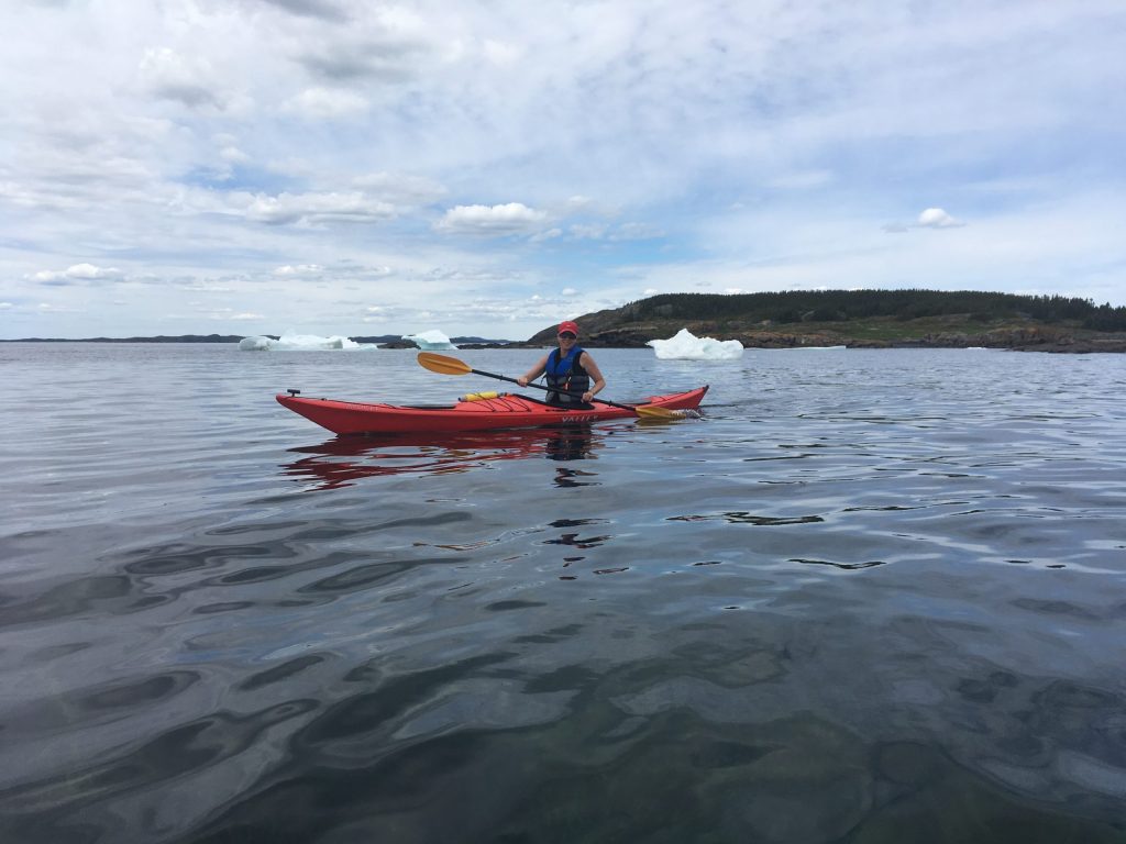 Woman sea kayaking with iceberg in background